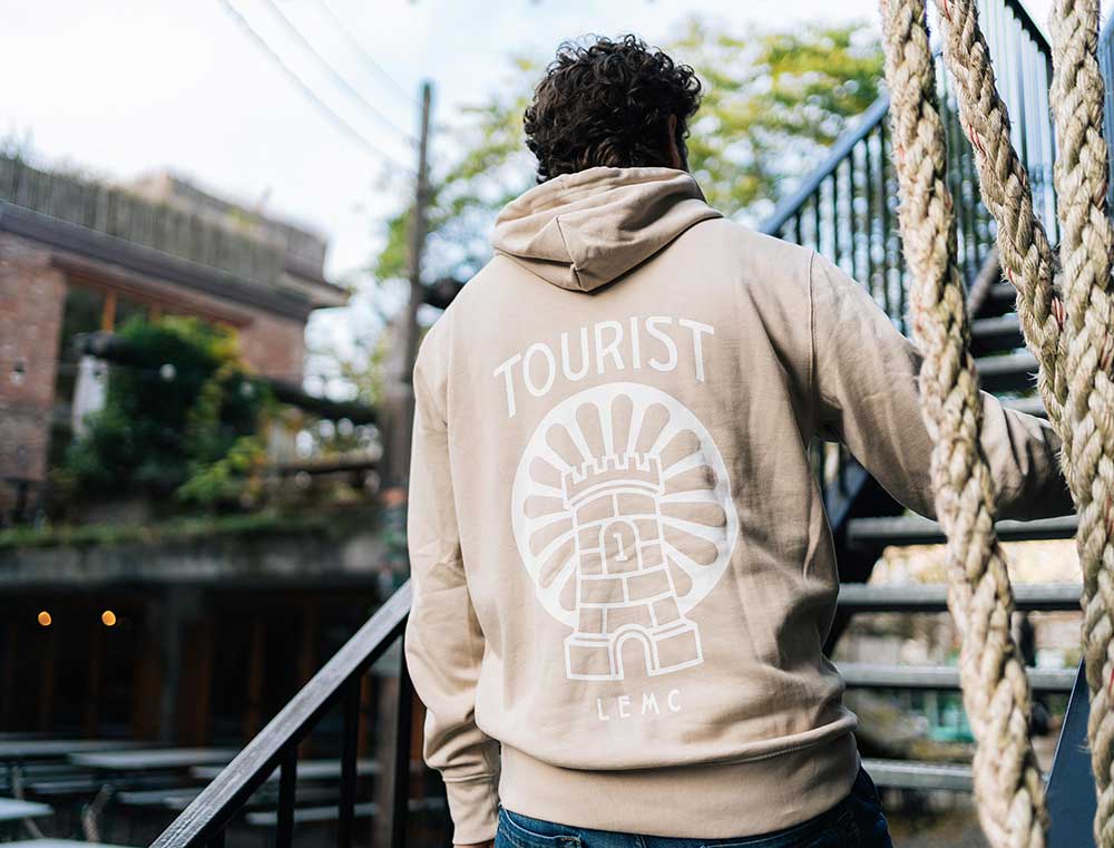 Een man met de achterkant van een zandkleurige hoodie met een illustratie.