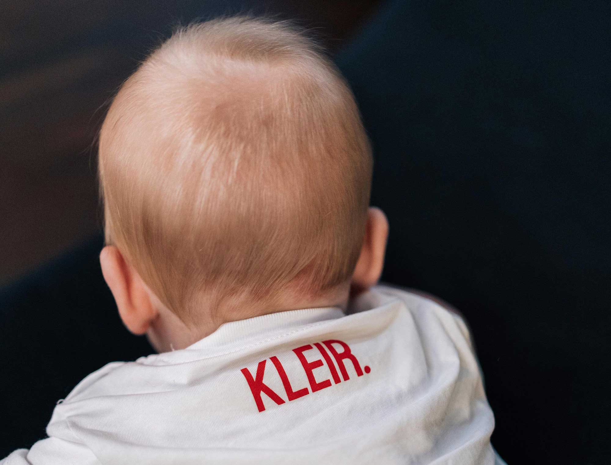 Baby met een witte T-shirt met KLEIR. op de achterkant 