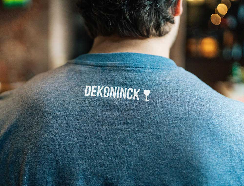 Achterkant van een blauwe T-shirt met het logo van De Koninck.