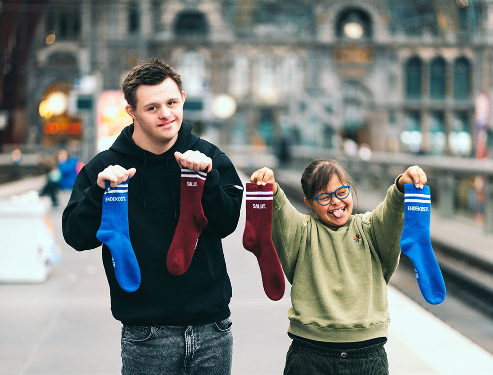 Twee kinderen met in hun handen twee verschillende sokken met opdruk SALUT. ENDEKOST.