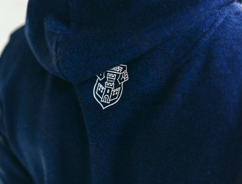 Close-up van logo van Tourist op een donkerblauwe hoodie.