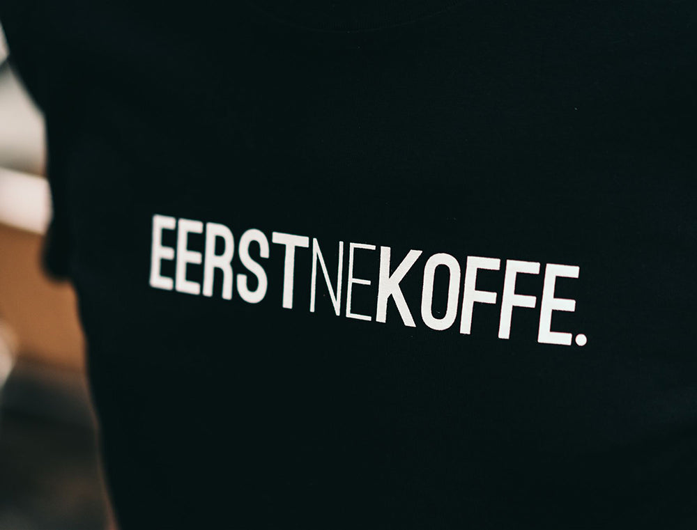 Close-up van zwarte T-shirt met opdruk EERSTNEKOFFE.