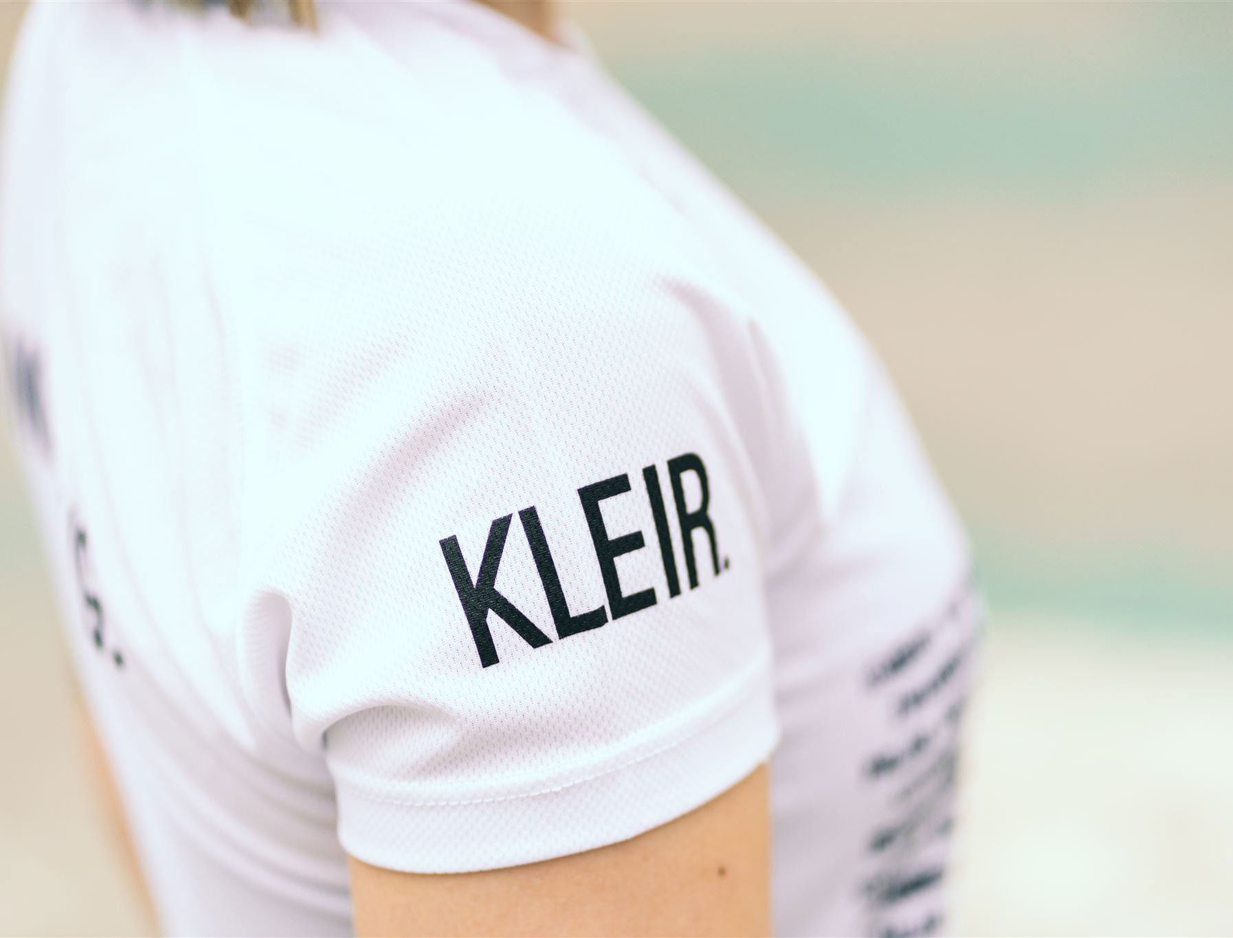 Close-up van een wit loopshirt met KLEIR. op de mouw.