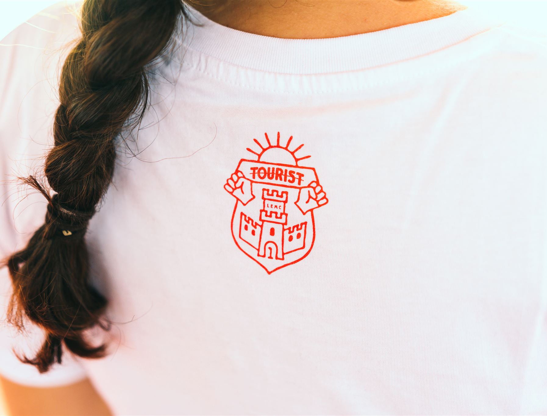 Rood logo van Tourist LeMC op een witte T-shirt.