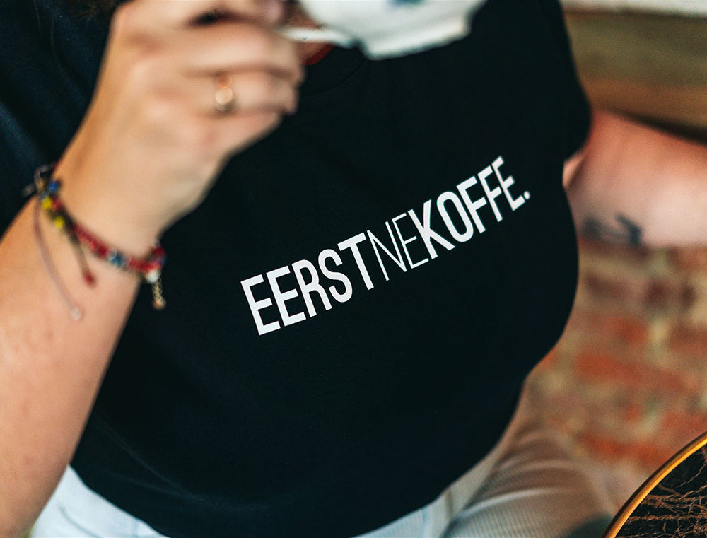 Close-up van zwarte T-shirt met opdruk EERSTNEKOFFE.