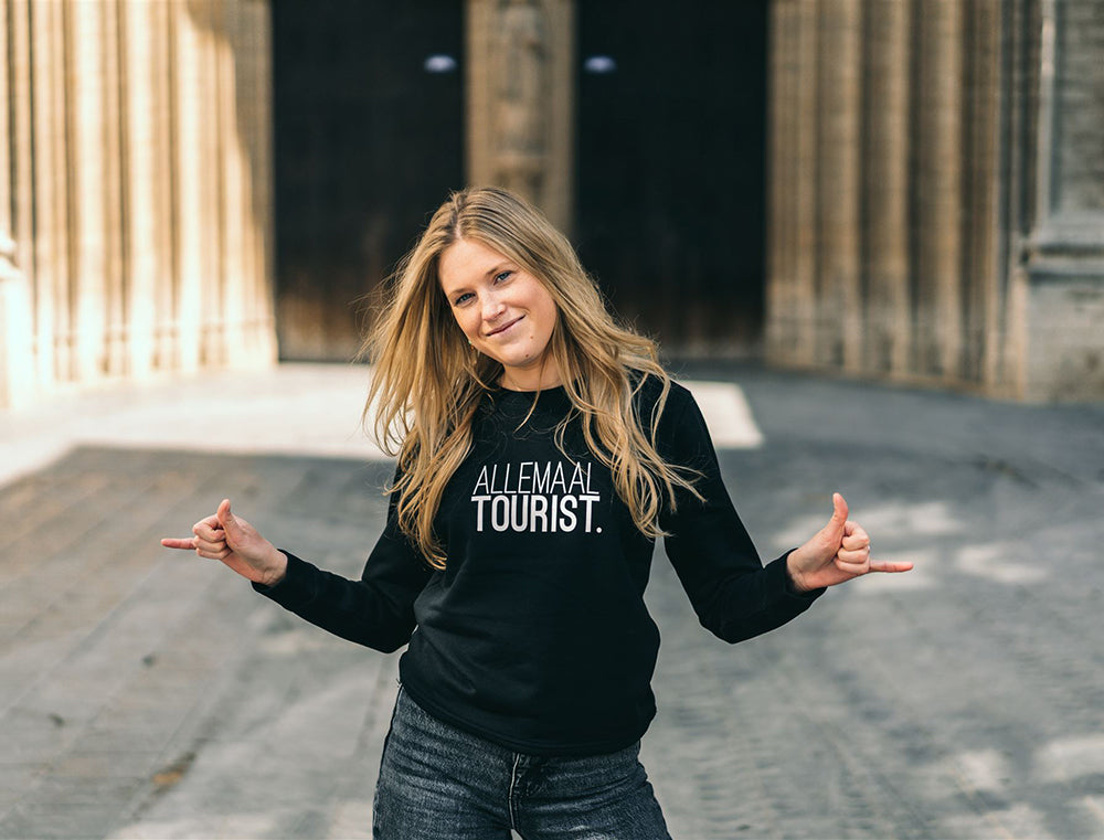 Vrouw met zwarte trui met opdruk 'ALLEMAALTOURIST.'