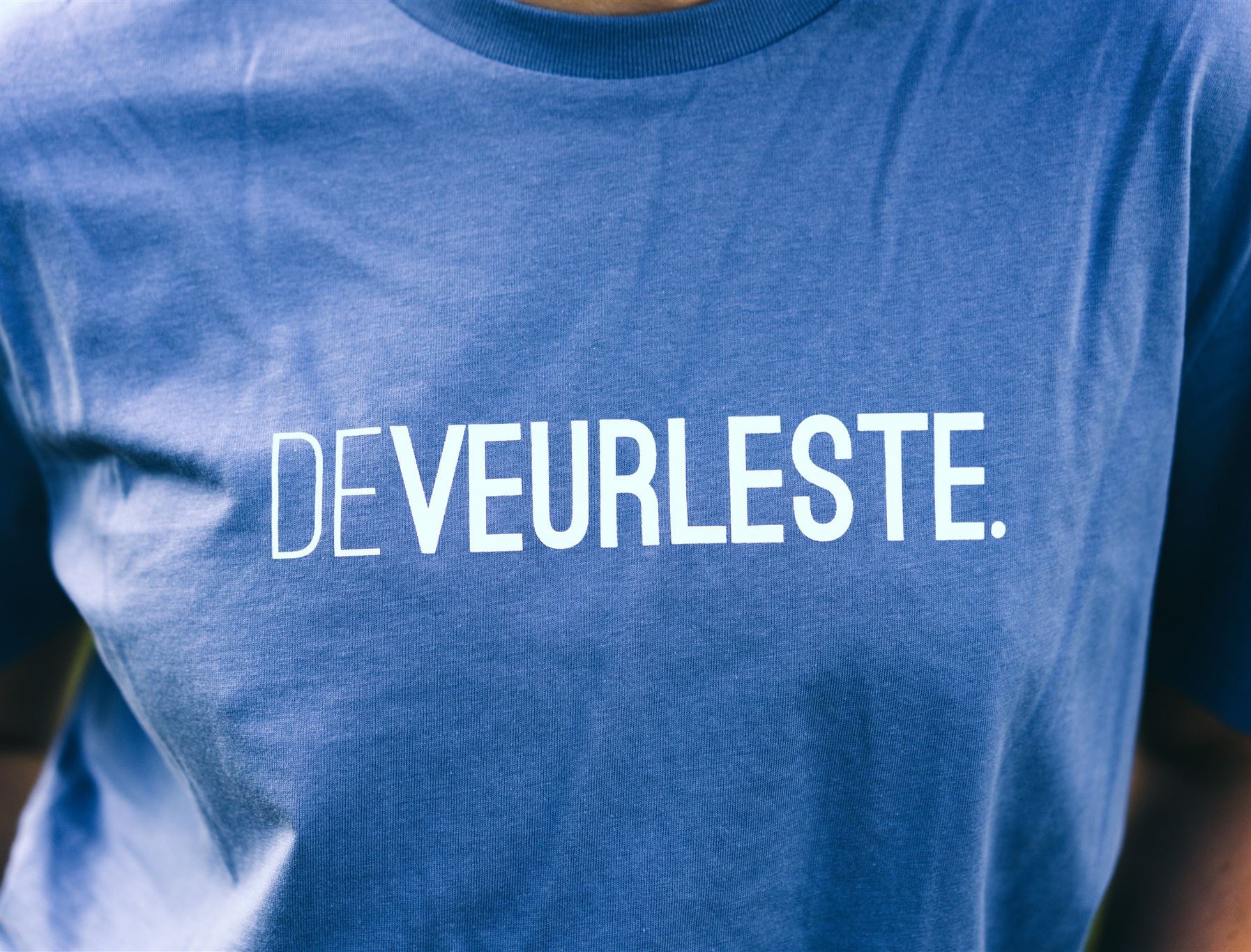 Close-up van een blauwe T-shirt met opdruk DEVEURLESTE.