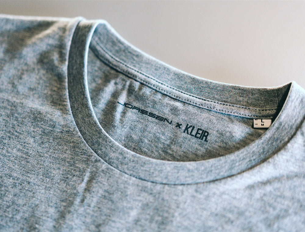Close-up van een grijze T-shirt met de logo's van Jorssen en KLEIR.