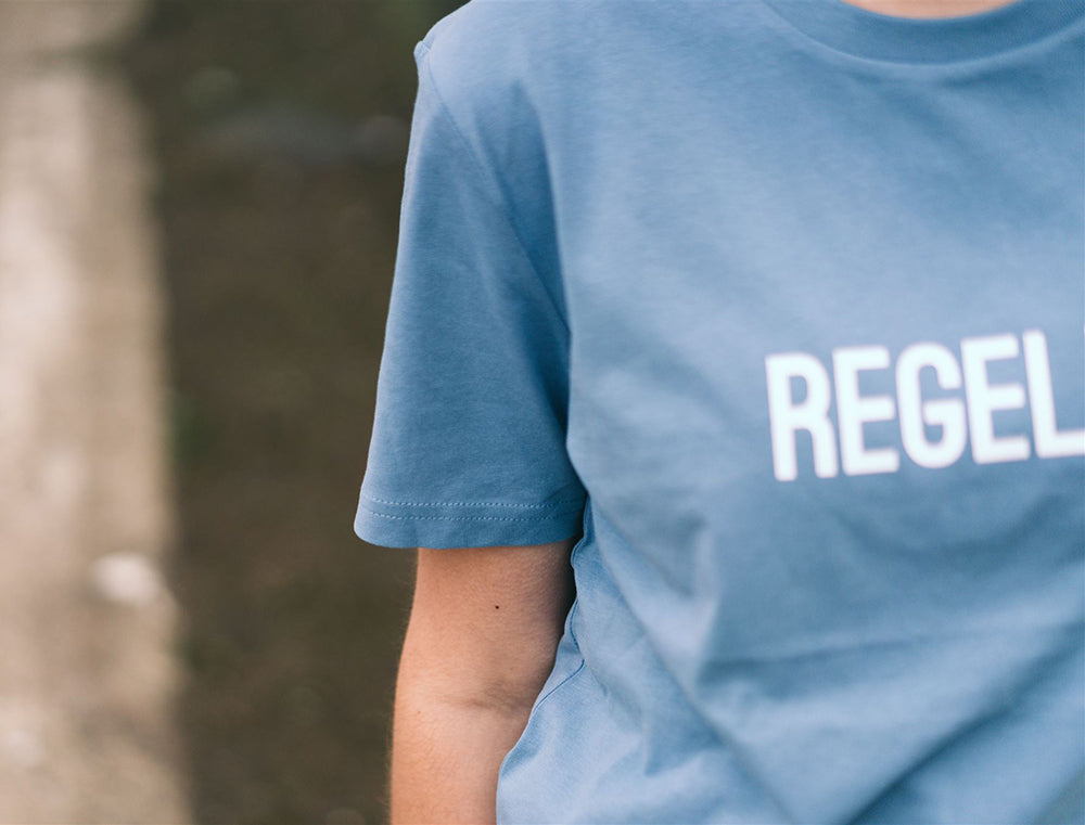 Close-up van een lichtblauwe T-shirt met opdruk REGELET.