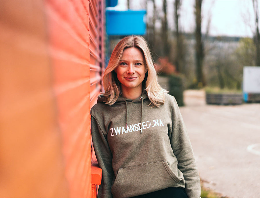 Vrouw met kaki hoodie met opdruk ZWAANSDEGIJNA.
