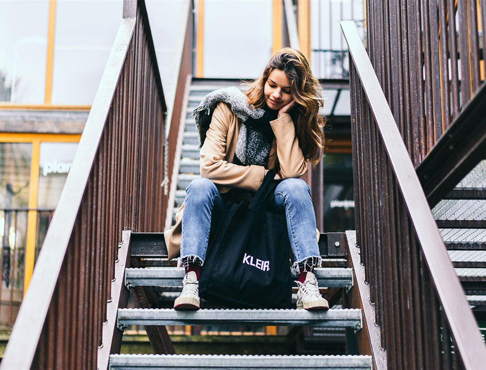Vrouw met zwarte totebag met opdruk KLEIR.
