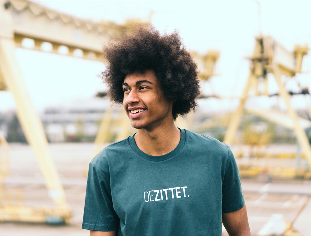 Man met petrolblauwe T-shirt met opdruk OEZITTET.