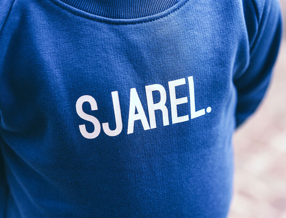Close-up van blauwe trui met opdruk SJAREL.