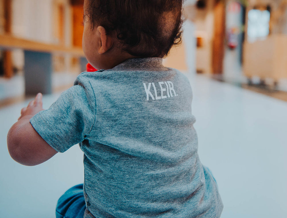 Close-up van grijze baby T-shirt met opdruk KLEIR. in de nek.