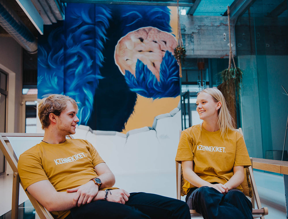 Man en vrouw met oker-kleurige T-shirt met opdruk KZENNEKIKET.