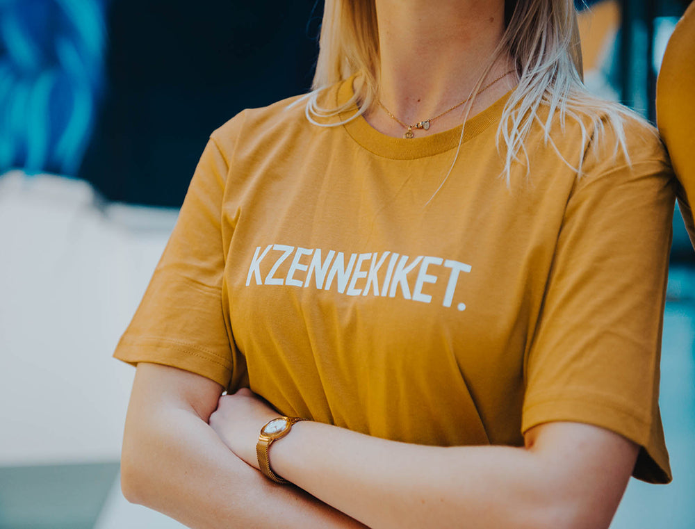 Vrouw met oker-kleurige T-shirt met opdruk KZENNEKIKET.