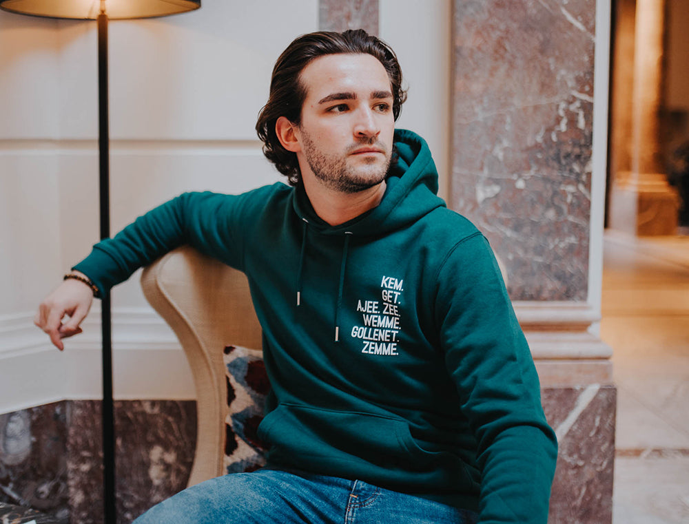 Man met groene hoodie met de vervoeging van het werkwoord HEBBEN als opdruk.