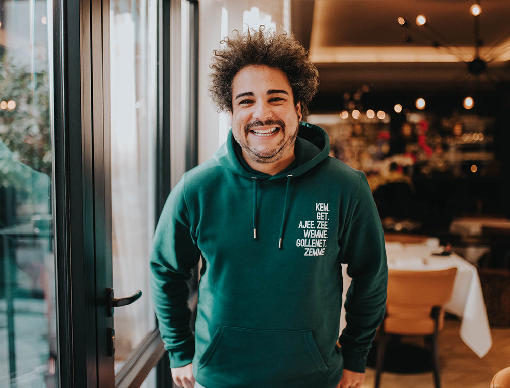 Man met groene hoodie met de vervoeging van het werkwoord HEBBEN als opdruk.