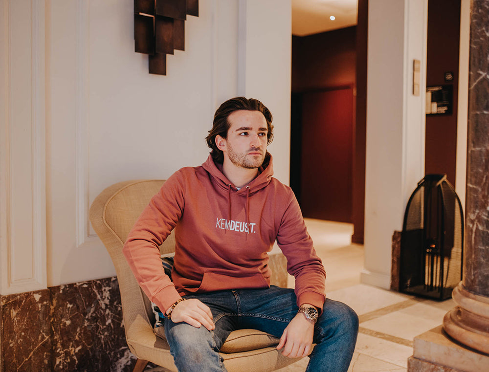 Man met een bordeaux hoodie met opdruk KEMDEUST.
