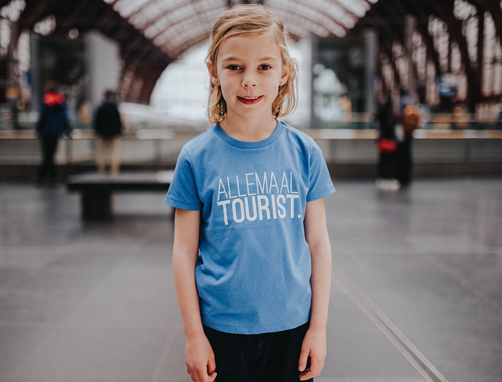 Meisje met blauwe T-shirt met opdruk ALLEMAALTOURIST.