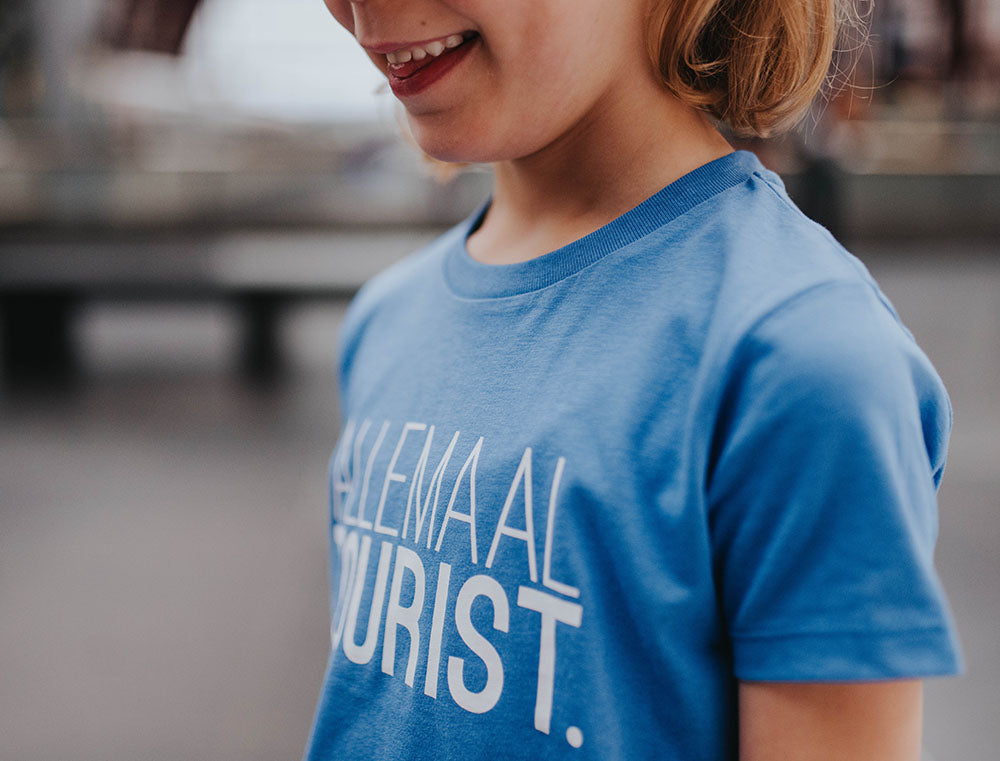 Close-up van blauwe T-shirt met opdruk ALLEMAALTOURIST.