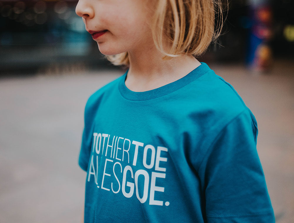 Close-up van een blauwe T-shirt met het opdruk TOTHIERTOEALLESGOE.