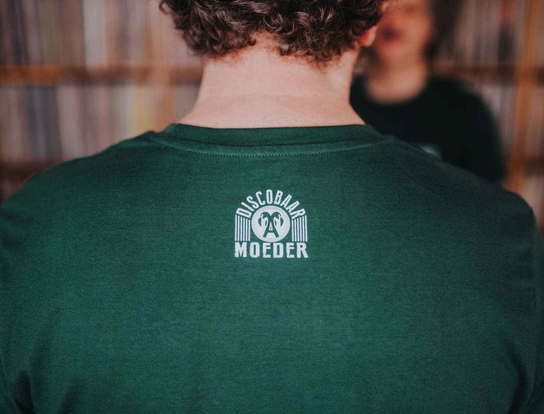 Close-up van het logo van Discobaar a moeder op een groene T-shirt.